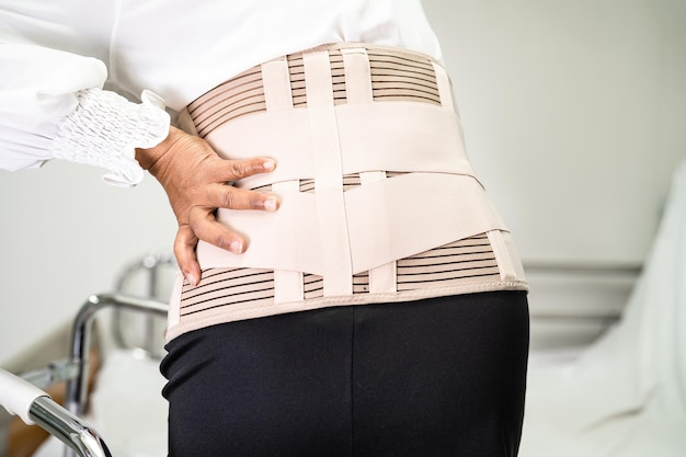 Asiatische Patientin trägt Rückenschmerzstützgürtel für orthopädische Lendenwirbelsäule mit Gehhilfe