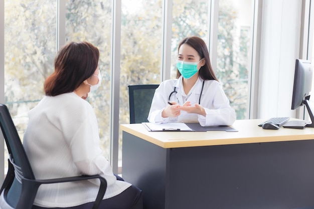 Asiatische professionelle Ärztin spricht mit ihrem Patienten, während sie im Krankenhaus eine medizinische Gesichtsmaske trägt