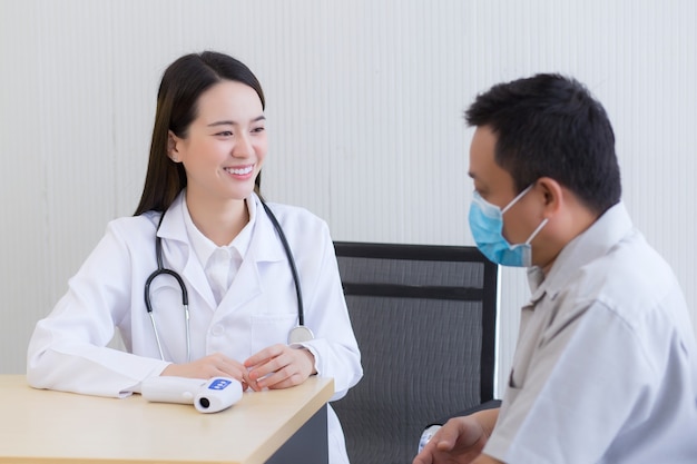 Asiatische Ärztin spricht und ermutigt mit einem Mannpatienten, sich im Krankenhaus um seine Gesundheit zu kümmern.