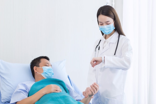 Asiatische Ärztin überprüft den Puls eines männlichen Patienten, indem er sein Handgelenk im Krankenhaus berührt