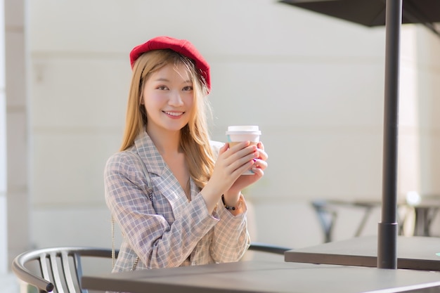 Asiatische schöne Frau, die Anzug und rote Mütze mit bronzenen Haaren trägt, sitzt auf einem Stuhl im Café?