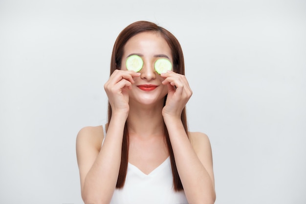 Asiatische schöne Frau, die Gurkenstücke auf ihre Augen aufträgt.