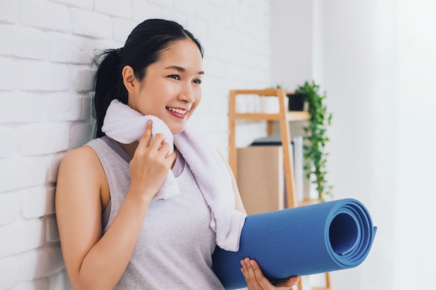 Asiatische schöne Frau, die Yogamatte nach dem Spielen Yoga ruht und hält