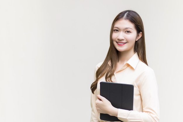 Asiatische schöne Frau mit langen Haaren, die ein langärmeliges Hemd trägt, hält Tablet-Smilie und glücklich auf weißem Hintergrund.