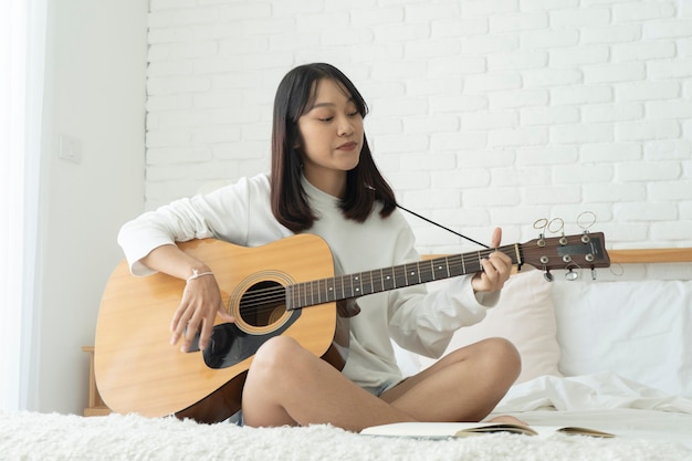 Asiatische schöne Frau spielt Gitarre auf ihrem Bett