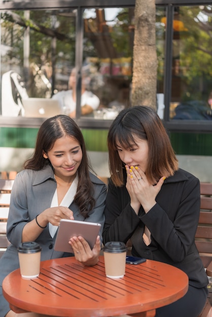 Asiatische schöne Geschäftsfrau, die mit Tablette und Smartphone im Kaffeecaféshop arbeitet