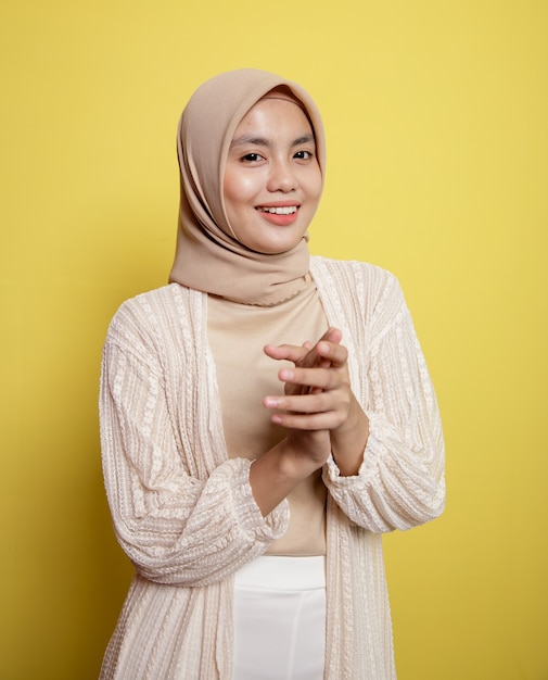 Asiatische schöne Hijab-Frau, die Handlächeln Ausdruck sehr glücklich lokalisiert auf einem gelben Hintergrund hält
