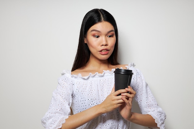 Asiatische schöne junge frau des porträts, die mit einem wegwerfglas des spaßgetränks lokalisierten hintergrund aufwirft