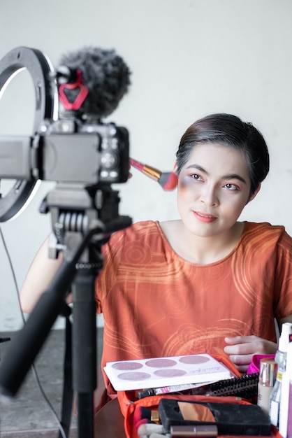 Asiatische schöne Mode-Beauty-Bloggerin untersucht eine Digitalkamera. bewertet Schönheitsprodukte für einen Videoblog und spricht über Kosmetik, während sie eine Makeup-Palette hält, während sie ihr Video aufnimmt.