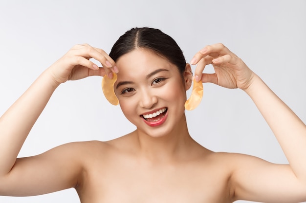 Asiatische Schönheitsjugendfrau pflegt ihre Haut mit Goldaugenmaskenflecken unter den Augen