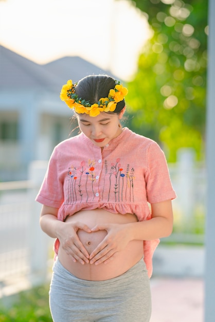 Asiatische schwangere Frau, die ein rosa Gewand trägt und glücklich lächelt