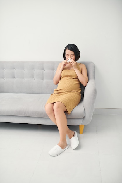 Asiatische schwangere Frau, die einen Husten und ein kaltes Fieber hat, die auf Sofa zu Hause sitzen