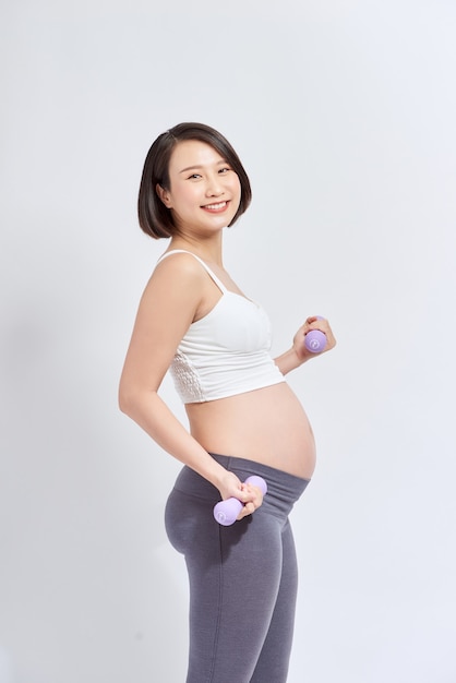 Asiatische schwangere Frau trainiert, steht und hebt Hanteln, sportliches Schwangerschaftsmutterschaftskonzept