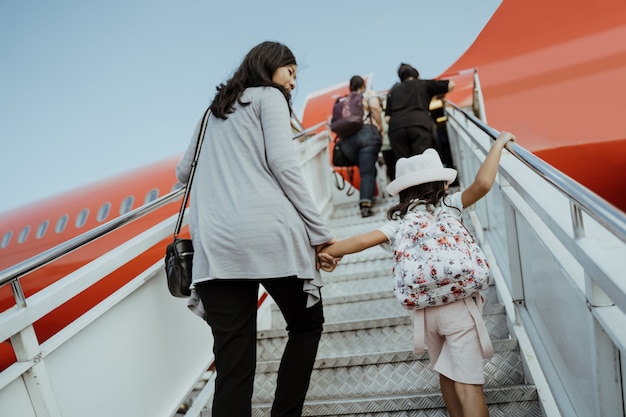 Asiatische schwangere Frauen und ihre Töchter gehen die Flugzeugtreppe hinauf