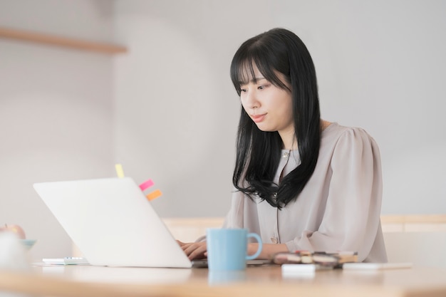 Asiatische schwarzhaarige Frau, die von zu Hause aus mit einem Laptop arbeitet