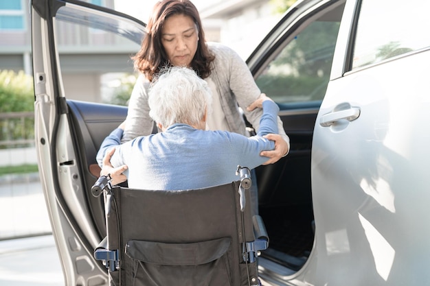 Asiatische Seniorin oder ältere Patientin der alten Dame, die im Rollstuhl sitzt, bereitet sich darauf vor, zu ihrem Auto zu gelangen, gesundes, starkes medizinisches Konzept