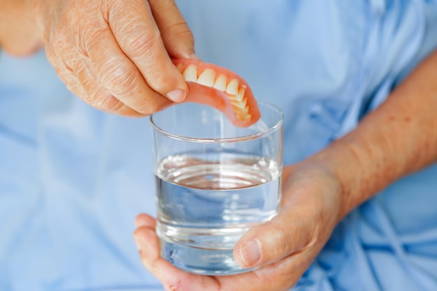 Asiatische Seniorin, Patientin, saubere Zahnprothese in einem Glas mit Lösung zum Kauen