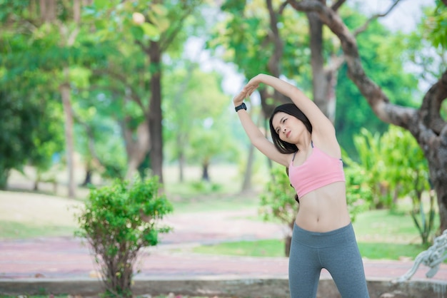 Asiatische sportliche Frau, die den Körper dehnt und frische Luft im Park atmetThailänderFitness- und Bewegungskonzept