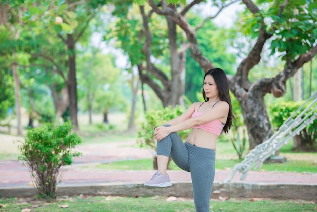 Asiatische sportliche Frau, die den Körper dehnt und frische Luft im Park atmetThailänderFitness- und Bewegungskonzept