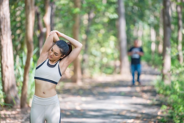 Asiatische sportliche Frau, die sich den Körper ausdehnt und frische Luft im Park atmetThailänderFitness- und BewegungskonzeptJoggen im Park