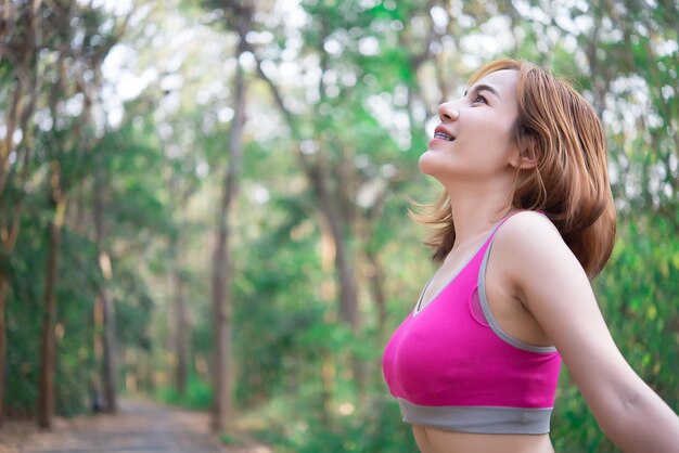 Asiatische sportliche Frau, die sich die Arme streckt und frische Luft im Park einatmetThailand Menschen trainieren Konzept