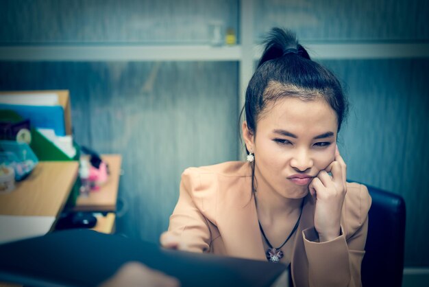 Asiatische stressgeschäftsfrau im offiziererhält harte arbeit von der chefin, die handberührungskopf verwendet