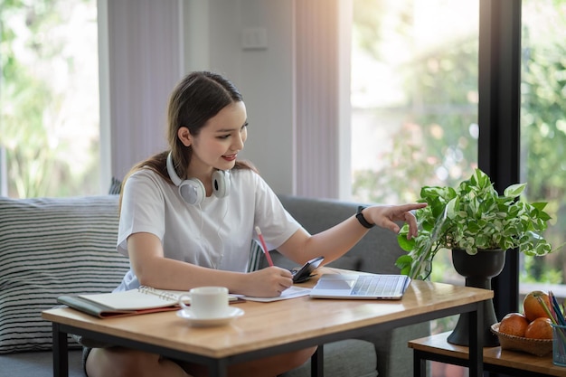 Asiatische Studentin macht sich zu Hause von einem Laptop aus Notizen zu einer Online-Studie