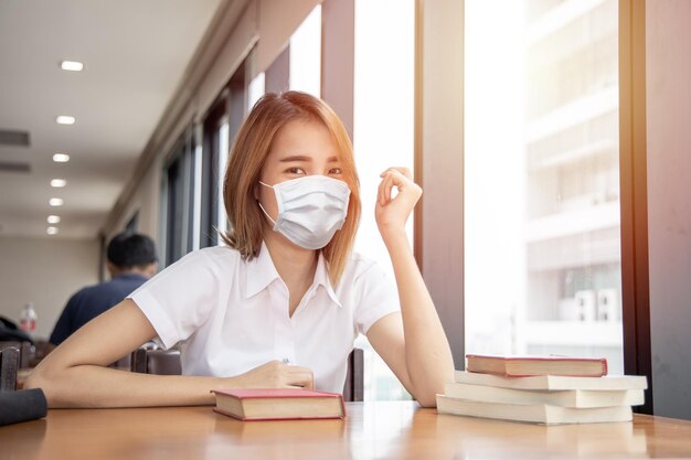 Asiatische thailändische Universitätsmädchen Teen Waring Gesichtsmaske für gesunde Vorbeugung von Covid in der Bibliothek.