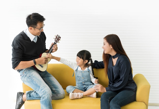 Asiatische Tochter, die Gitarre spielt und mit Vater und Mutter auf Sofa im Wohnzimmer singt.