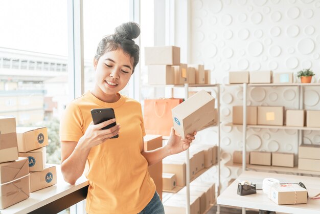 Asiatische Unternehmerin, die zu Hause mit Verpackungsbox am Arbeitsplatz arbeitet - Online-Shopping KMU-Unternehmer oder freiberufliches Arbeitskonzept