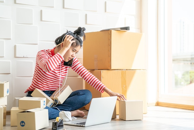 Asiatische Unternehmerin, die zu Hause mit Verpackungsbox am Arbeitsplatz arbeitet - Online-Shopping-KMU-Unternehmer oder Online-Verkaufskonzept