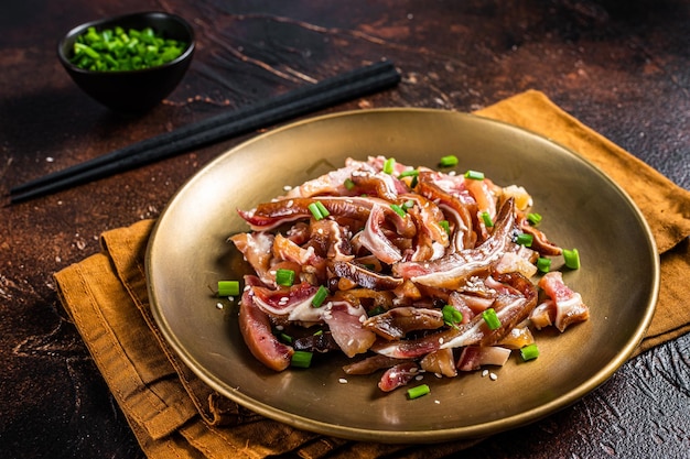 Asiatische Vorspeise Schweineohren mit Sesam, Frühlingszwiebeln und würziger Sauce Dunkler Hintergrund Ansicht von oben