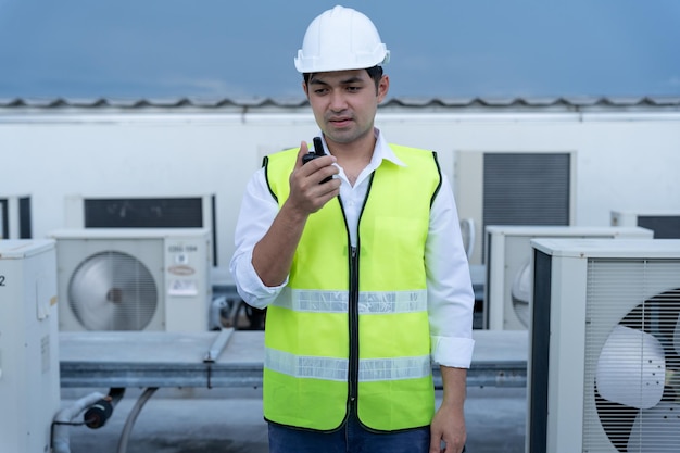Asiatische Wartungsingenieure arbeiten auf dem Dach eines Fabrikauftragnehmers, inspizieren das Kompressorsystem und planen die Installation von Klimaanlagen in der Walky-Talky-Wartung der Bautechnik