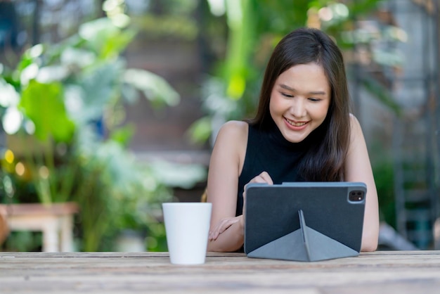 Asiatische weibliche digitale Nomadin Glück Freiheit fröhlich lächelnd Arbeiten mit Tablet im Garten outdoorasia Frau freiberuflich entspannen Freizeit überall arbeiten und reisen mit Garten Bokeh Hintergrund