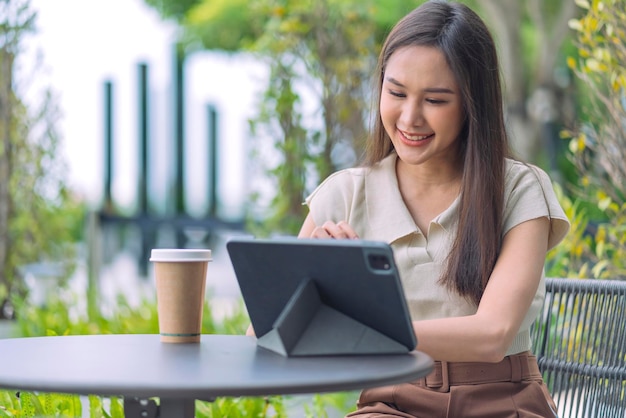 Asiatische weibliche digitale Nomadin Glück Freiheit fröhlich lächelnd Arbeiten mit Tablet im Garten outdoorasia Frau freiberuflich entspannen Freizeit überall arbeiten und reisen mit Garten Bokeh Hintergrund