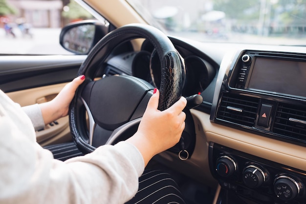 Asiatische weibliche Hände am Lenkrad eines Autos während der Fahrt mit Windschutzscheibe und Straße. Schwarze Frauenhände, die selbstbewusst ein Lenkrad halten. Hände am Steuer - Frau Autofahren - Asien