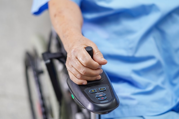 Asiatischer älterer Frauenpatient auf elektrischem Rollstuhl mit Fernbedienung am Krankenhaus.