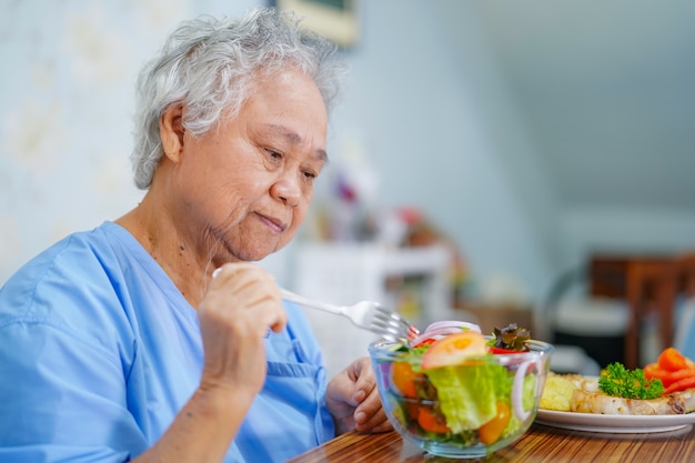 Asiatischer älterer Frauenpatient, der Frühstück im Krankenhaus isst.