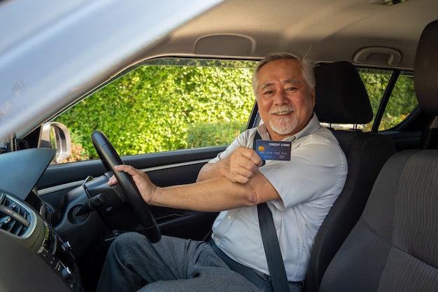 Asiatischer älterer Mann, der im Auto sitzt und Kreditkarte hält.