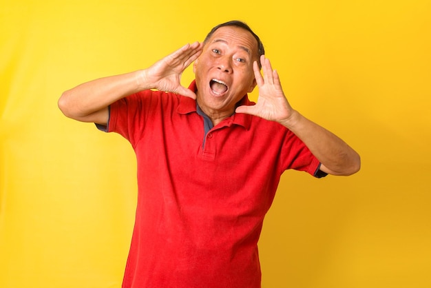 Asiatischer älterer Mann, der lässiges T-Shirt trägt, isoliert gelben Hintergrund, der laut mit schreit und schreit