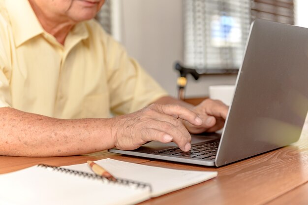 Asiatischer älterer Mann, der Laptop verwendet und nach einer Versicherung nach dem Ruhestand sucht. Großvater bleibt allein zu Hause.