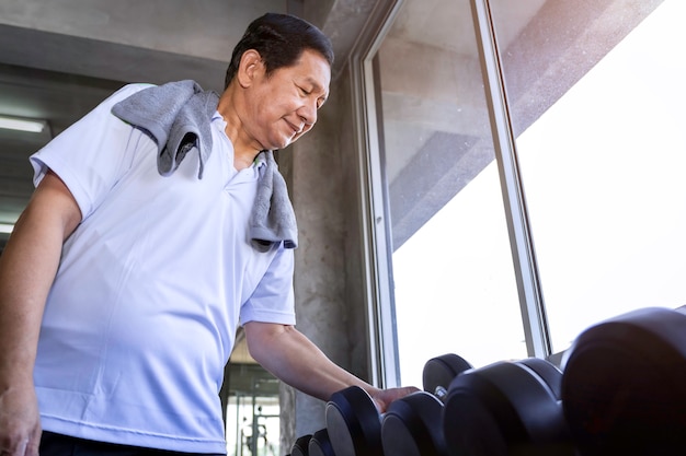 Asiatischer älterer Mann im Sportkleidungstraining mit Dummkopf an der Turnhalle.