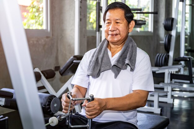 Asiatischer älterer Mann im Sportkleidungstraining mit Maschine an der Turnhalle.