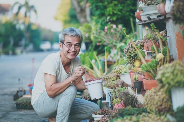 Asiatischer alter Mann, der sich im heimischen Garten um Zimmerpflanzen kümmert