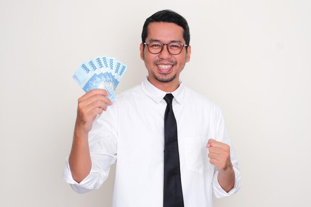 Asiatischer Angestellter ballte die Faust und zeigte ein glückliches Gesicht, während er Geld in der Hand hielt