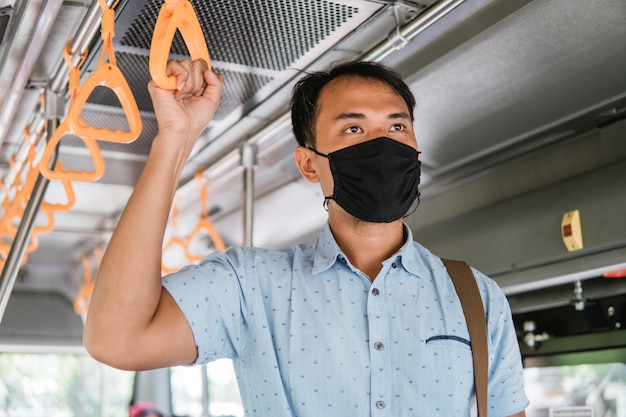 Asiatischer Angestellter, der eine Maske zum Schutz von Fahrgästen des öffentlichen Verkehrs in der Straßenbahn trägt