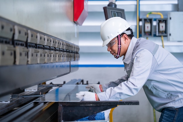 Foto asiatischer arbeiter, der einen sicherheitsanzug trägt und hydraulikmaschine einstellt