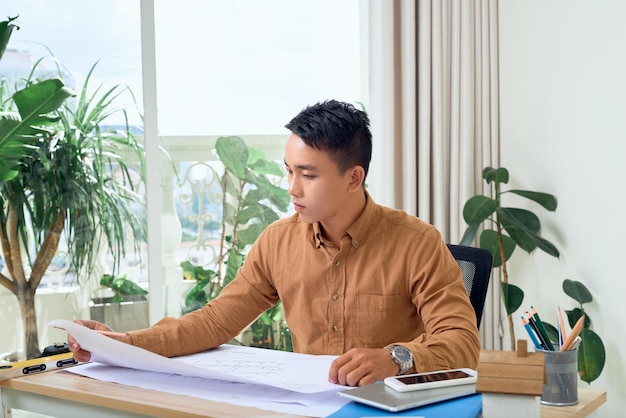 Asiatischer Architekt, der in seinem Büro an einer Blaupause arbeitet