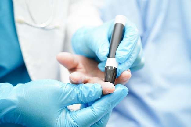 Asiatischer Arzt benutzt einen Lancet-Stift am Finger eines älteren Patienten, um den Blutzuckerspiegel der Probe zu überprüfen