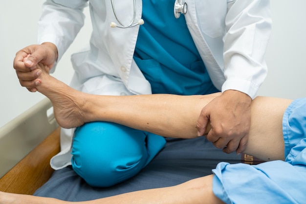Asiatischer Arzt Physiotherapeut untersucht, massiert und behandelt Knie und Bein eines älteren Patienten im Krankenschwesterkrankenhaus der orthopädischen Klinik.